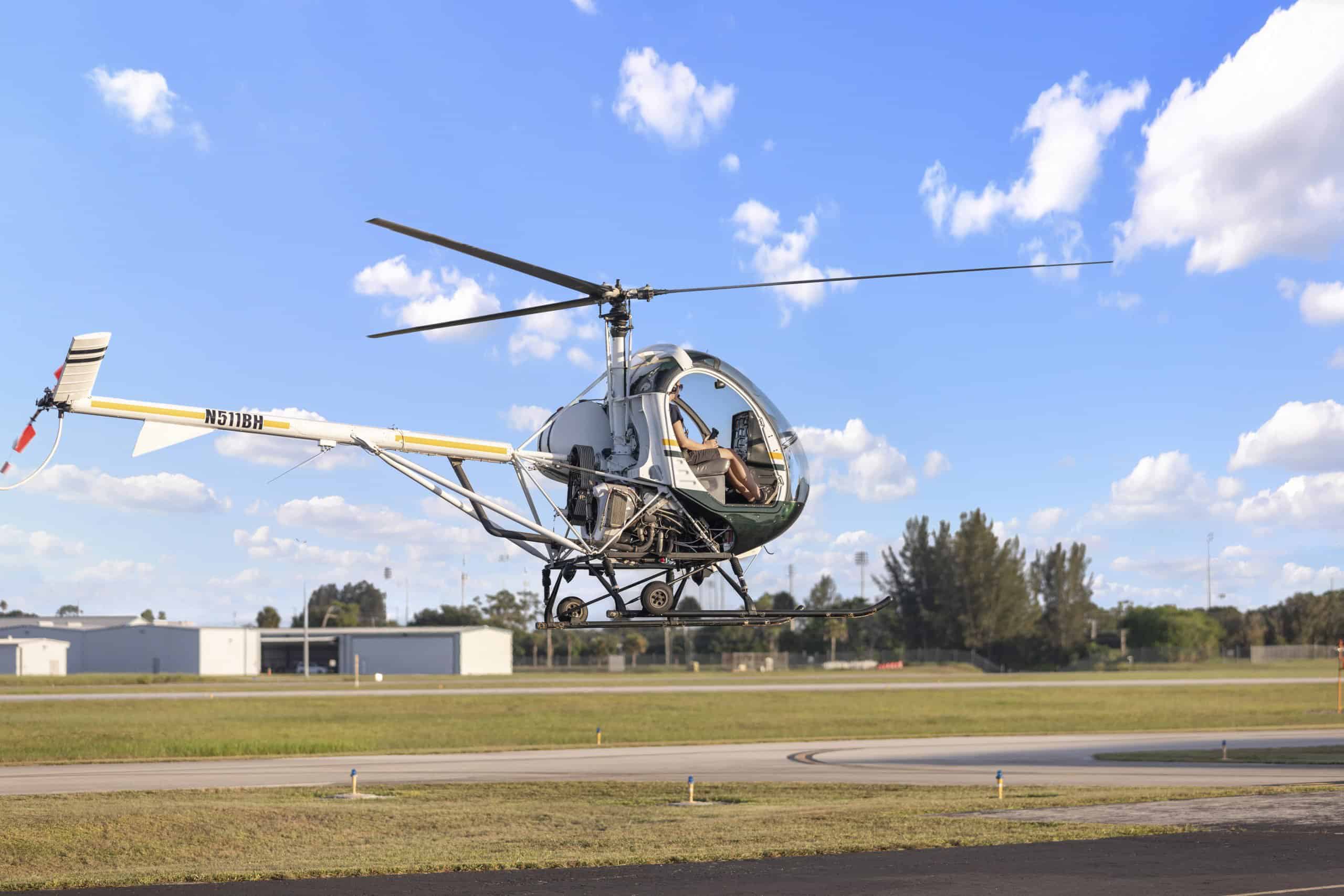 Photo of a helicopter hovering over a runway with low buildings in the background