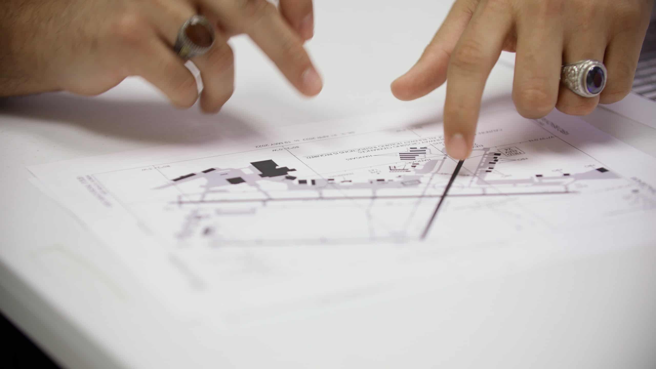 Photo of two people's hands pointing at a diagram on a desk