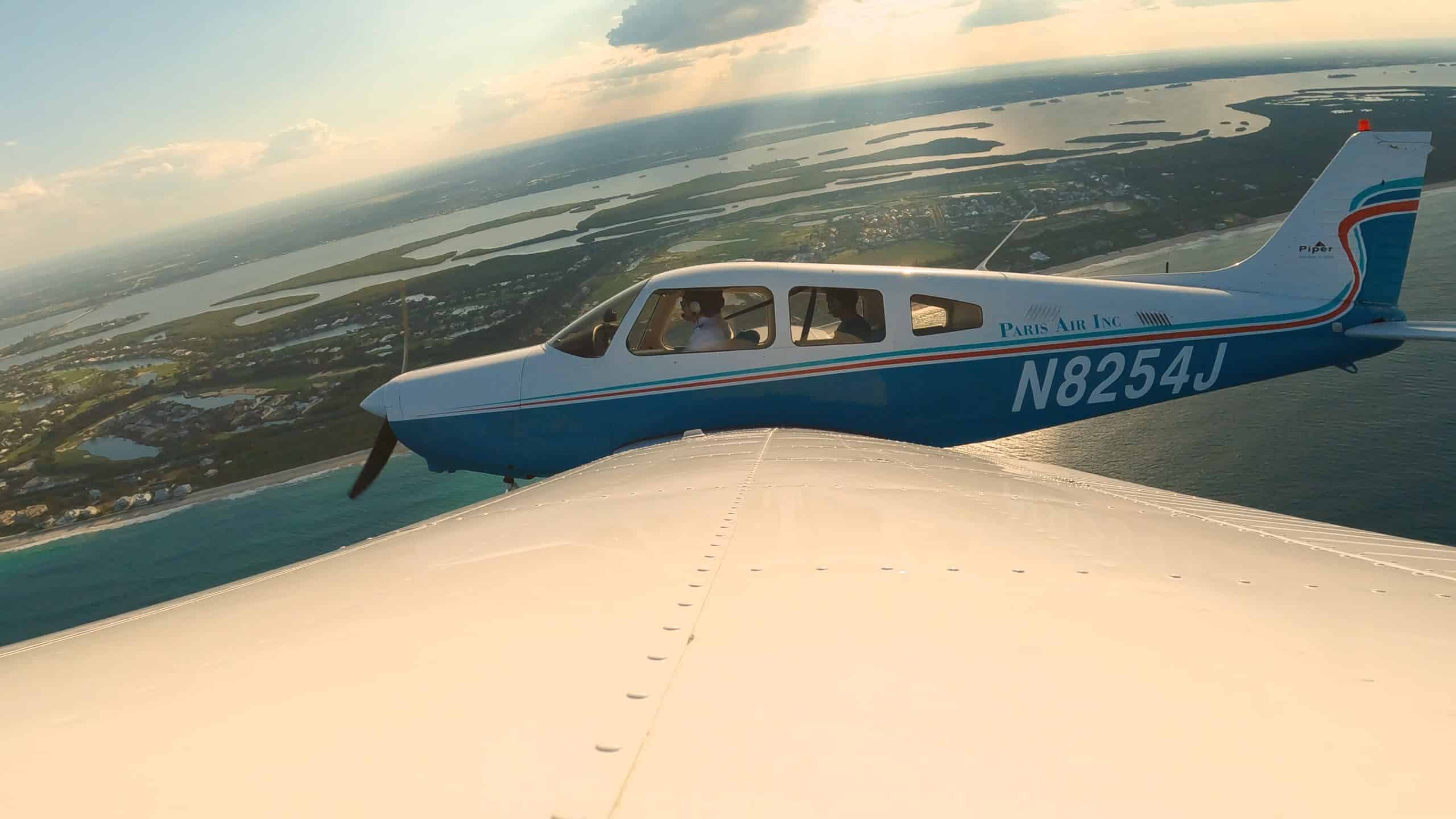 Small airplane viewed over its wing, with vista of water, land, and sky in the background