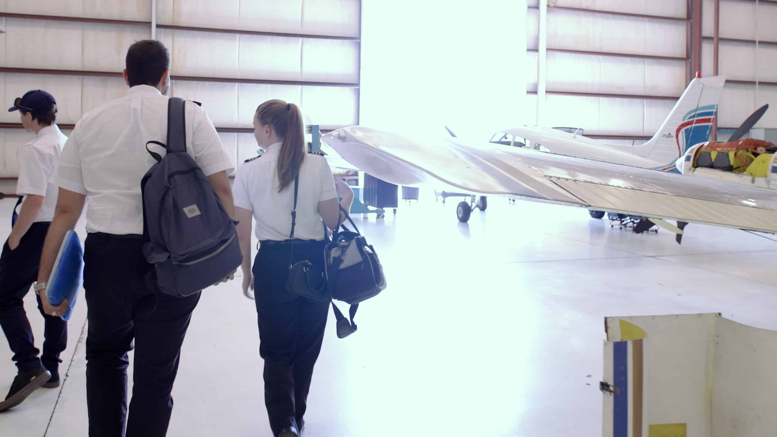Paris Air flight students walking in a hangar with a small plane in the background