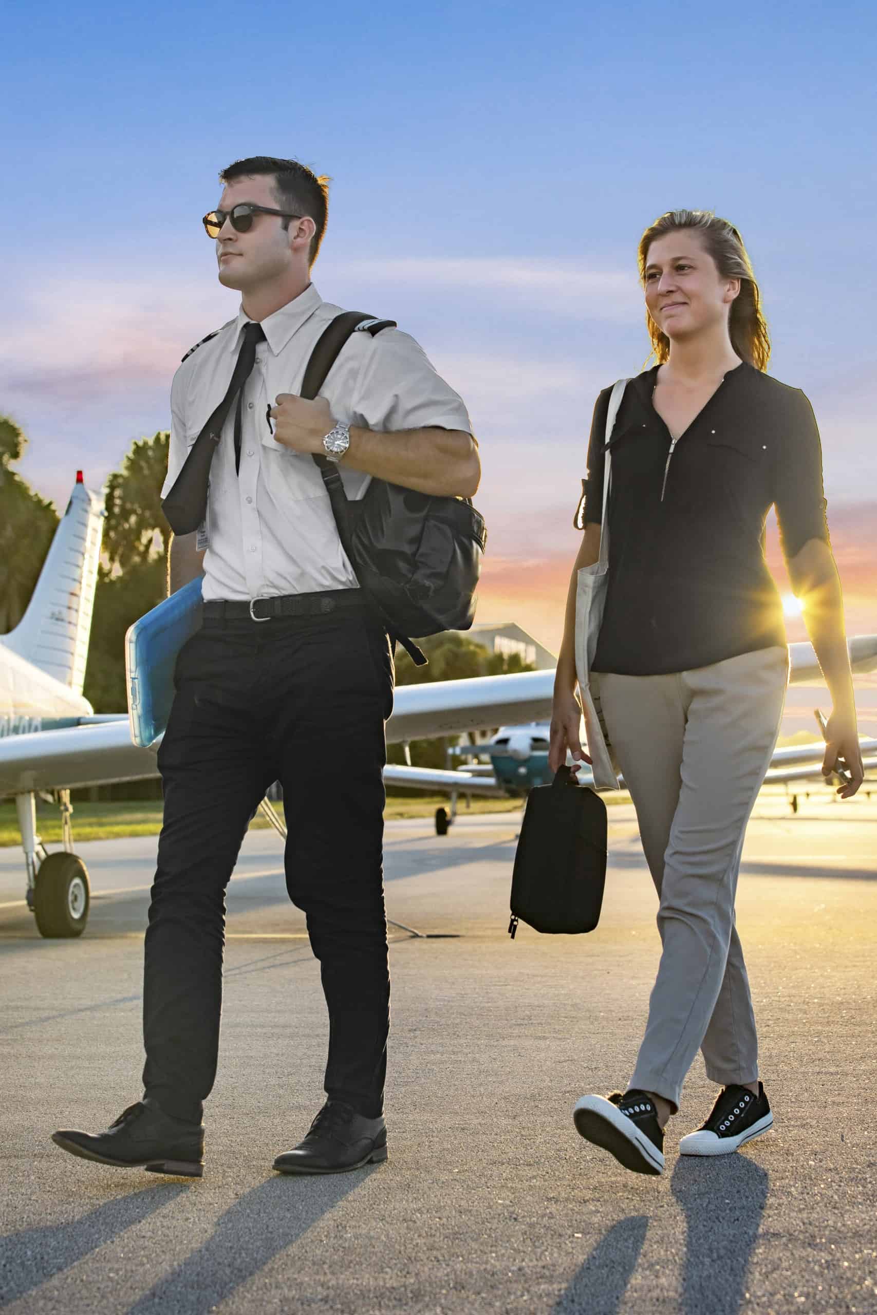 A pilot and passenger walking on the tarmac near small airplanes